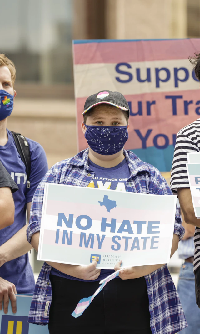 People standing together, holding signs with transgender flags and affirmative language at a rally