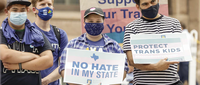 People standing together, holding signs with transgender flags and affirmative language at a rally