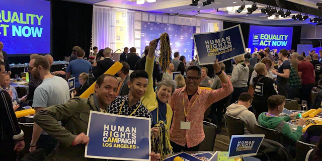 Four people standing together in a darkly lit room at a gala holding up HRC Los Angeles signs
