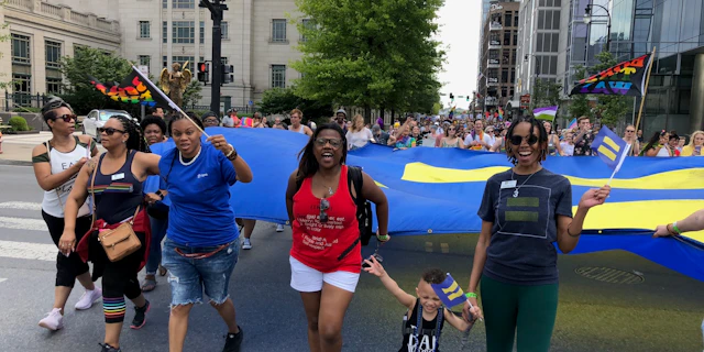 Group of people walking the in the middle of the street in a protest formation, holding HRC flags