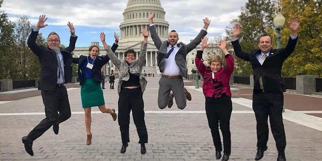 Five people outside the Capitol Building jumping in the air