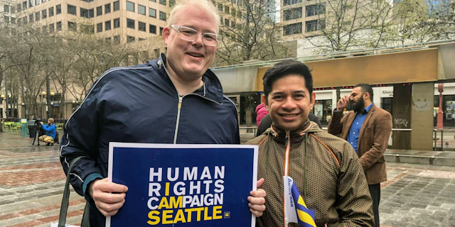 Two people standing together holding a HRC Seattle sign