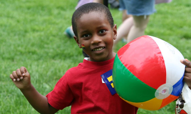 Black child playing on the grass with an inflated beach ball