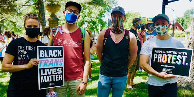 Four people standing outside in masks and holding up a sign that says Black Trans Lives Matter